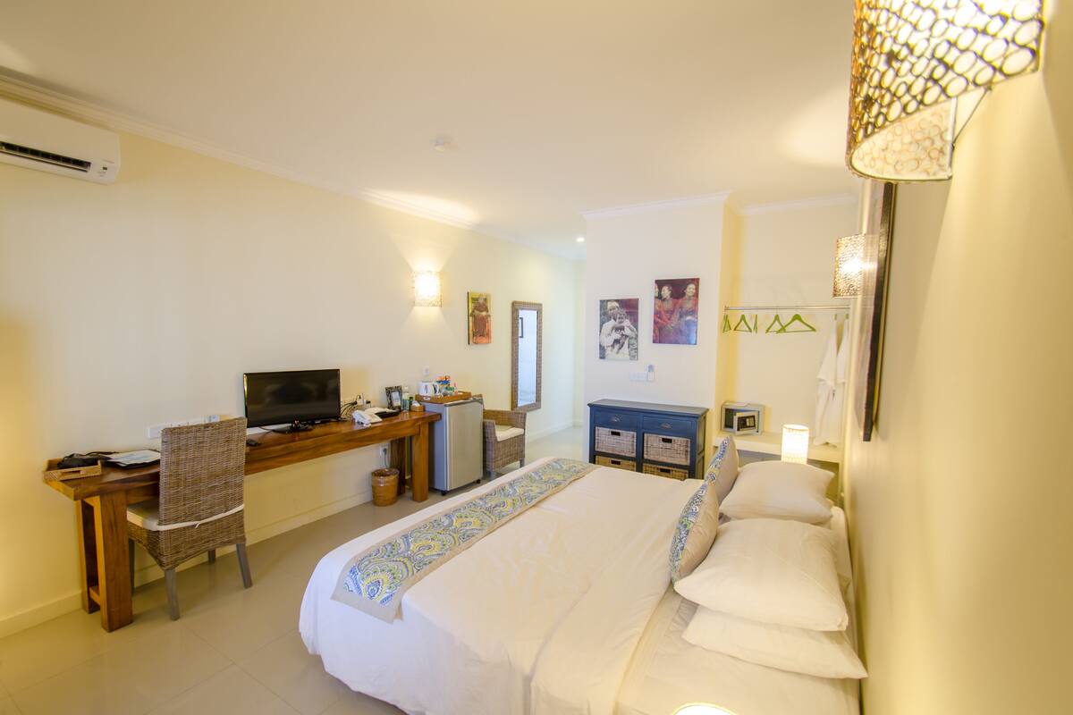 Une chambre d’hôtel comprenant un lit, un bureau avec une télévision, une chaise, un petit réfrigérateur et une salle de bain avec un miroir et un porte-serviettes.
