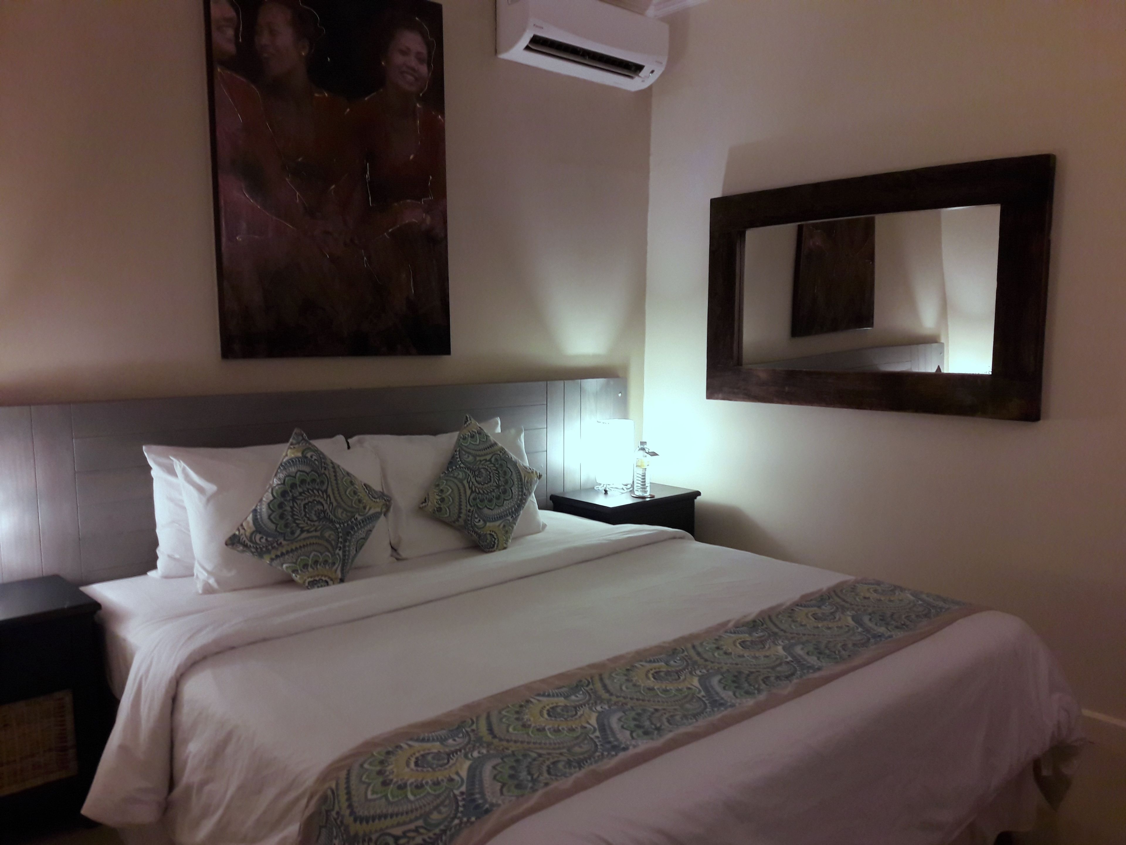 Habitación de hotel con una cama grande, una mesita de noche, un espejo montado en la pared y un equipo de aire acondicionado.