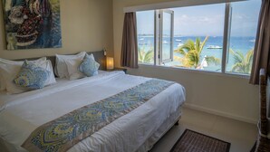 A hotel room with a large bed, a painting on the wall, a window with a view of the sea, and a nightlight. - Scallywags Resort (Gili Trawangan)
