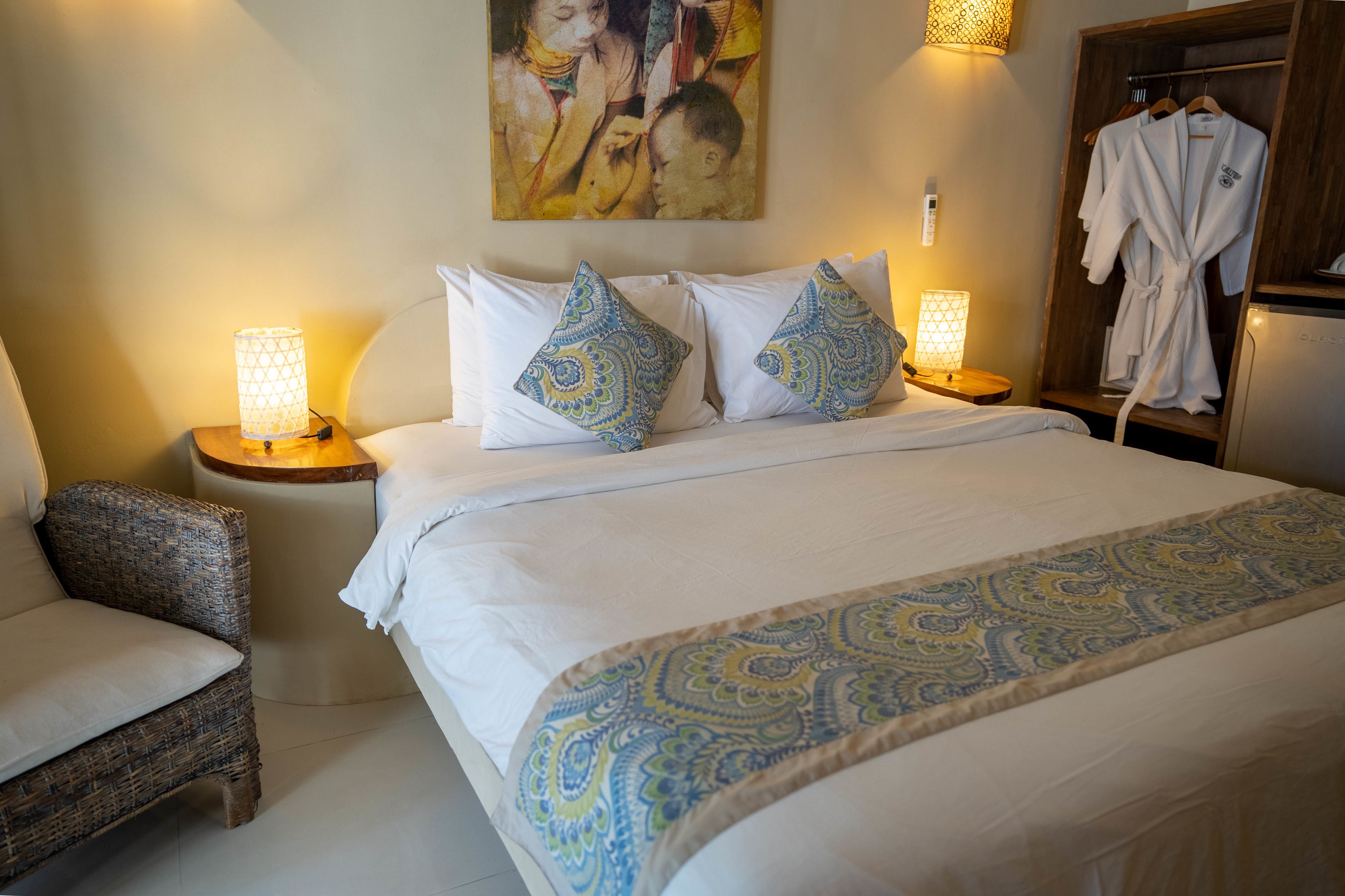 A hotel room with a large bed, two bedside lamps, a chair, and a robe rack.