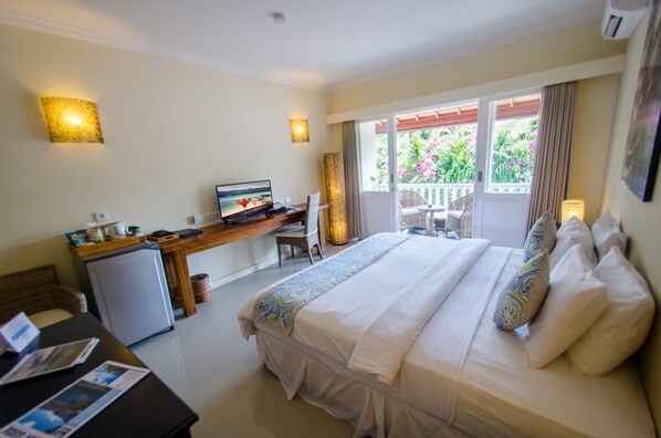 A hotel room with a bed, desk, and a small refrigerator. - Scallywags Resort (Gili Trawangan)