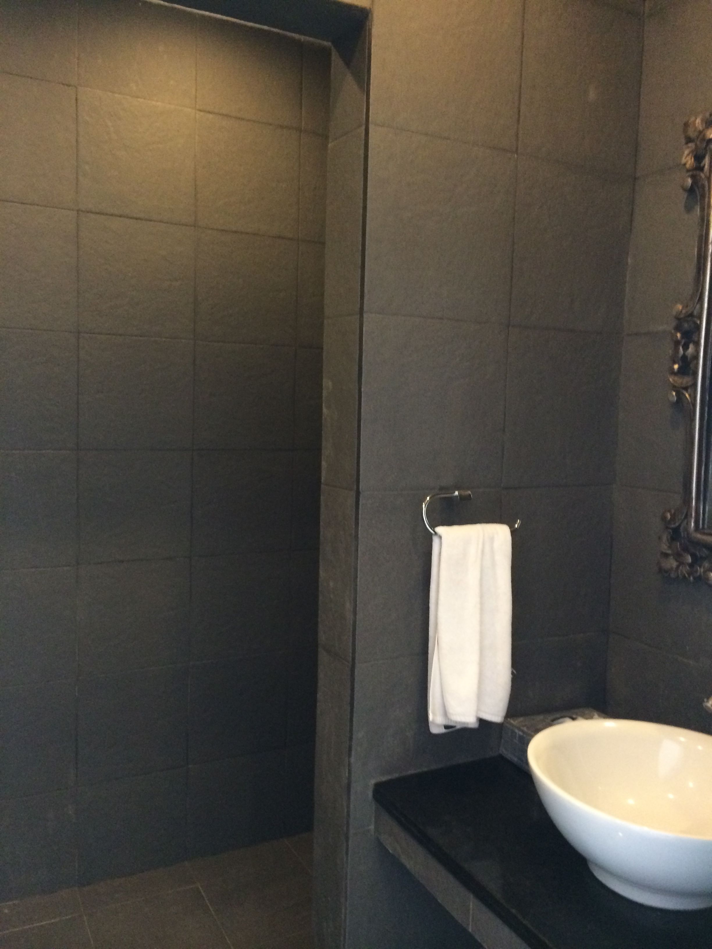 A modern bathroom with dark tiles, a white sink, and a towel rack.