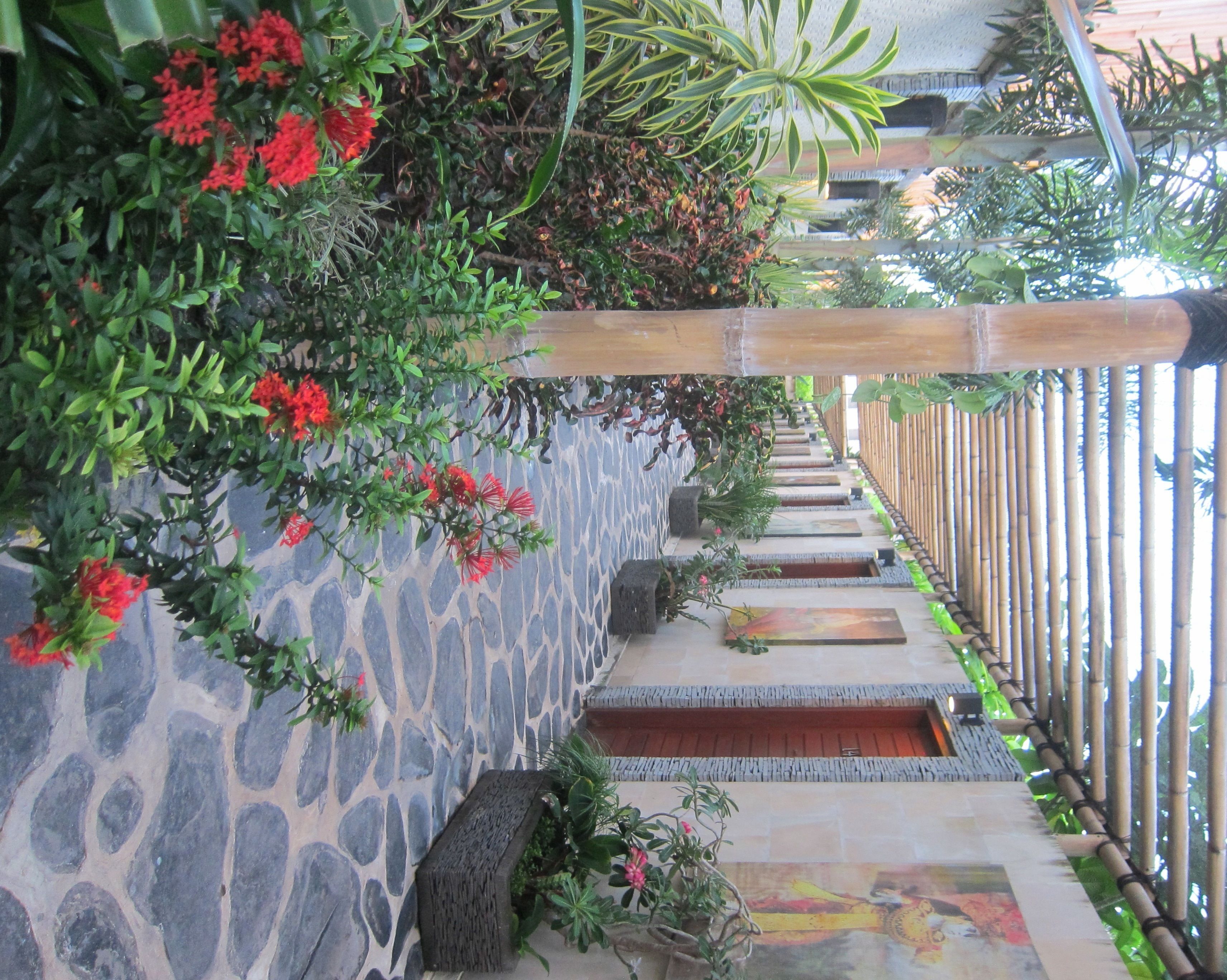 Una escalera de piedra con barandilla de bambú, rodeada de vegetación exuberante y flores rojas.