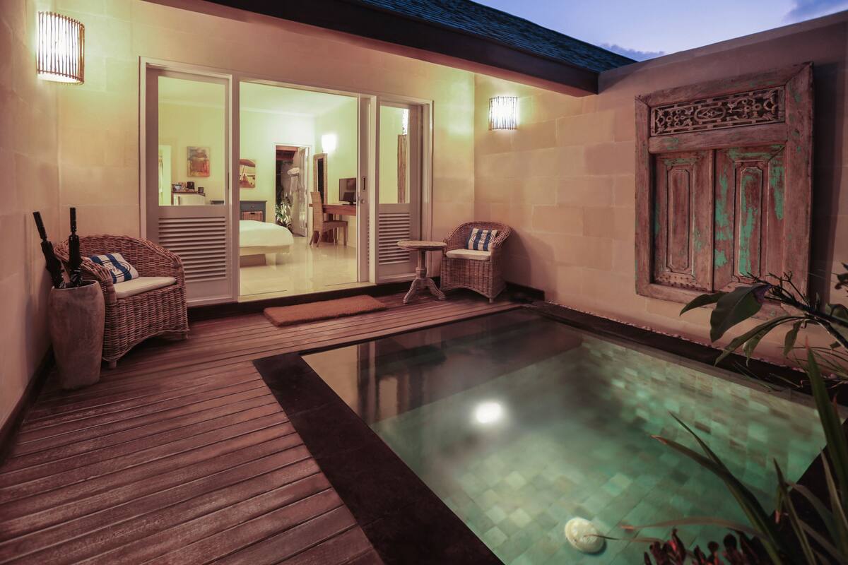 Un espace piscine doté d’une terrasse en bois, de chaises en osier et d’une pièce fermée par des parois vitrées, avec des portes coulissantes.