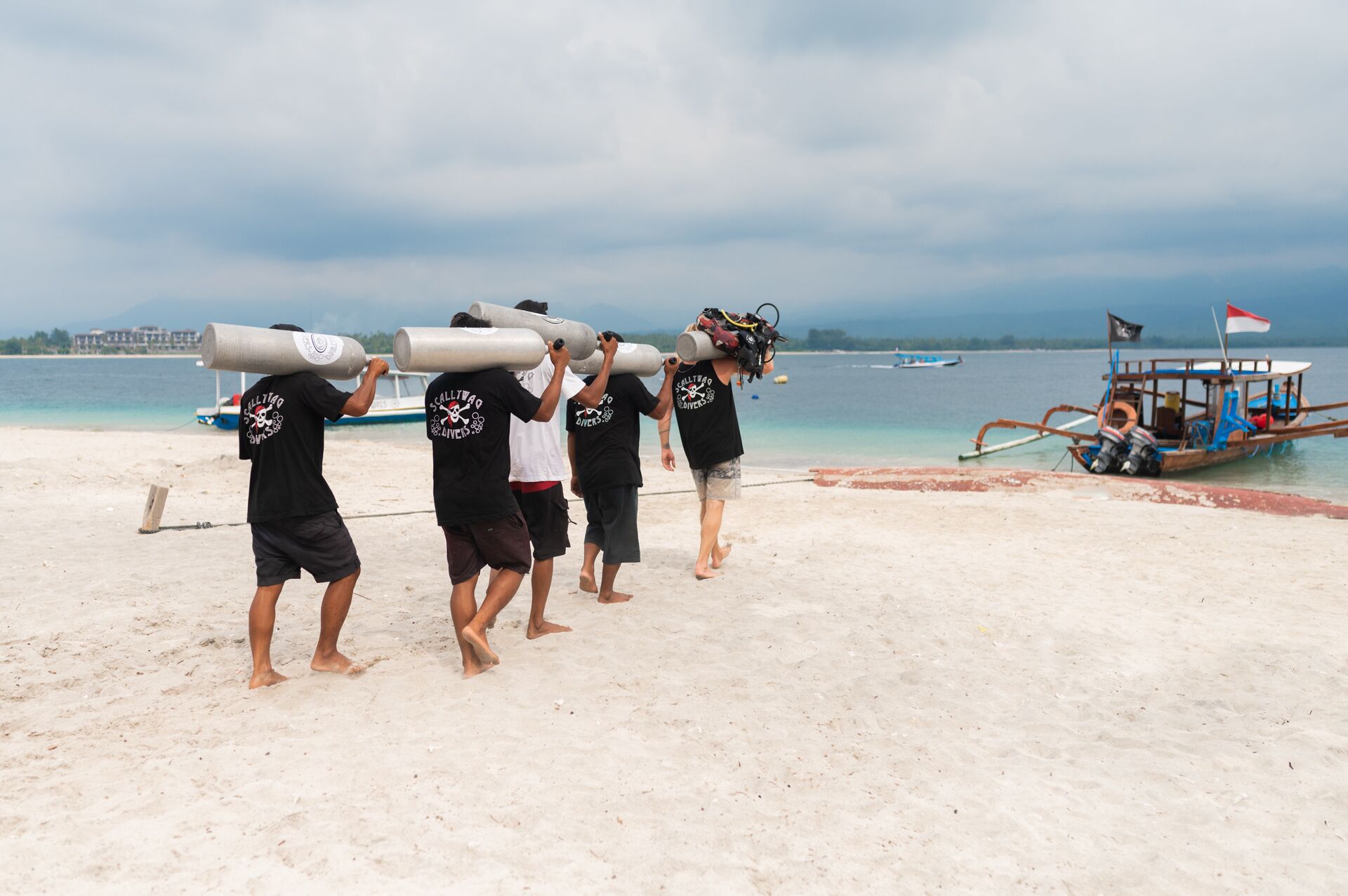 A group of people carrying large cylindrical objects on their shoulders on a beach.
