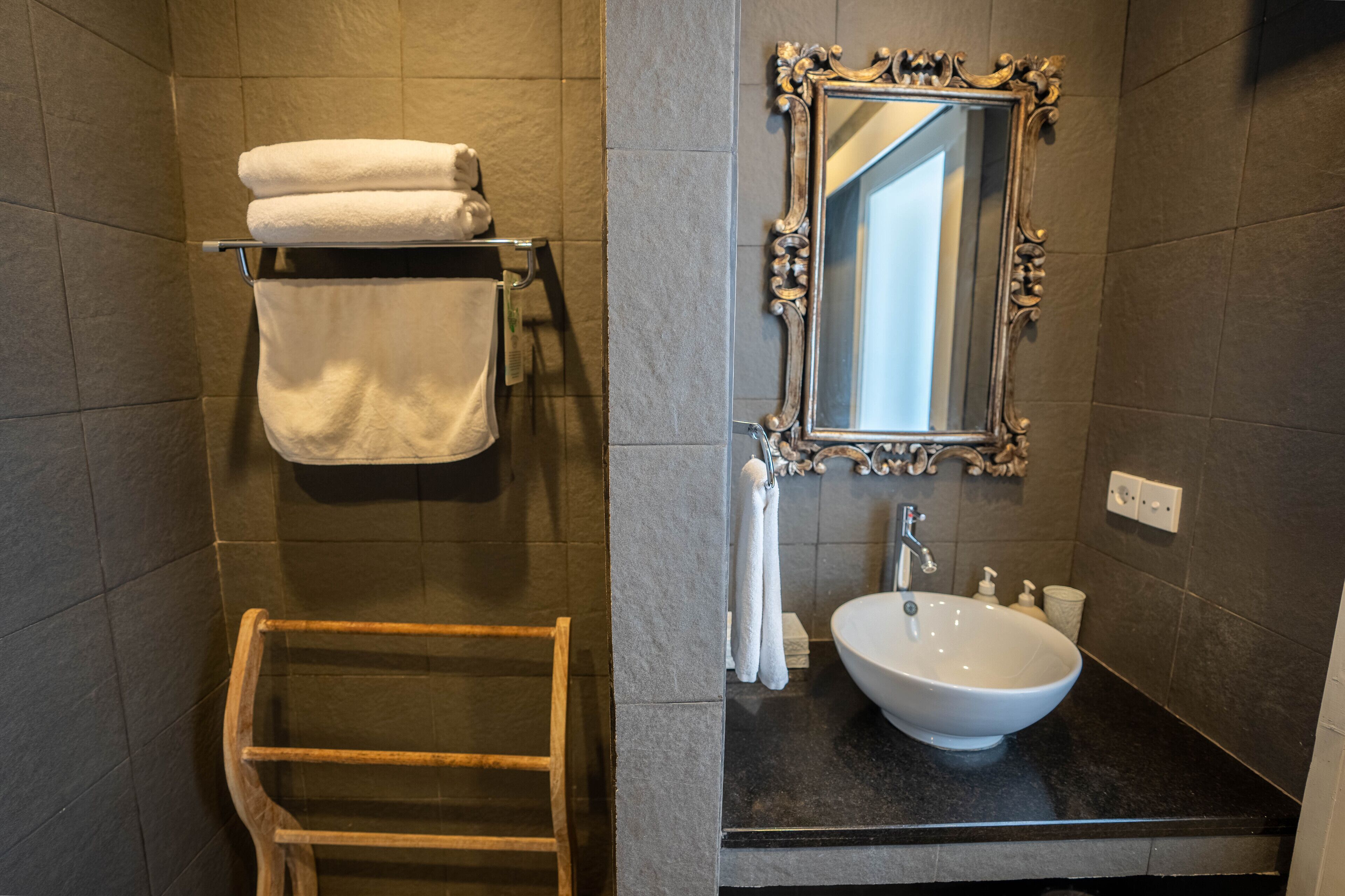 Une salle de bain avec un porte-serviettes en bois, un lavabo blanc et un miroir doté d’un cadre orné.