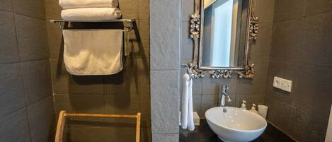Une salle de bain avec un porte-serviettes en bois, un lavabo blanc et un miroir doté d’un cadre orné.