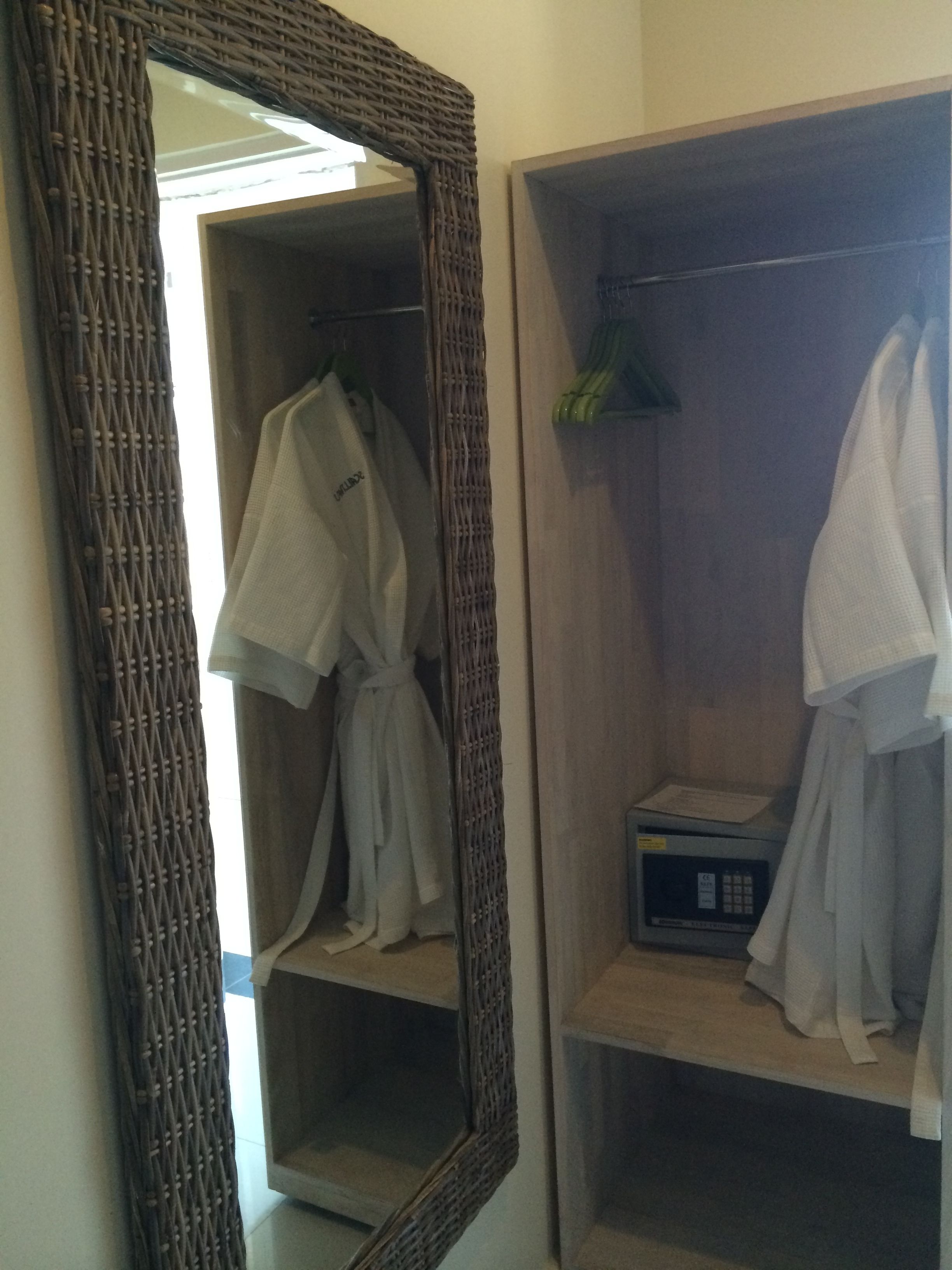 A bathroom with a large mirror, a wooden shelf, and two white robes hanging on hooks.