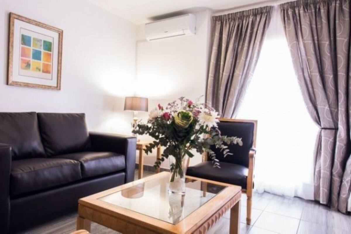 Un salón con un sofá de cuero negro, una mesa de centro de madera con un florero y una lámpara, además de un cuadro en la pared.