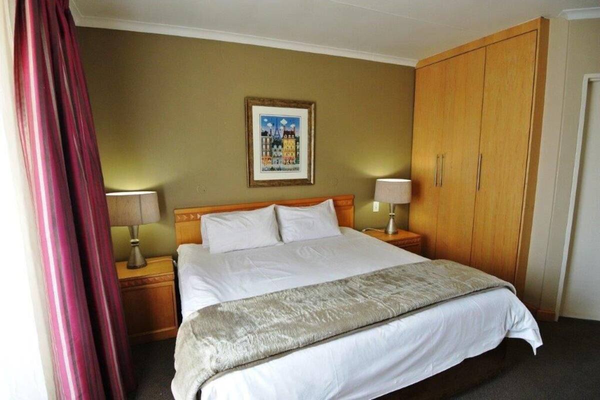 Habitación de hotel con cama, mesitas de noche, armario y un cuadro en la pared.