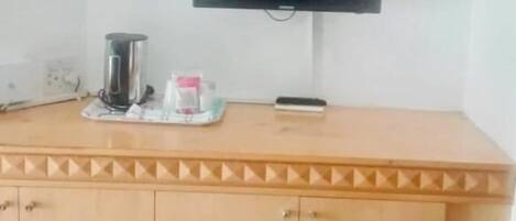 Une pièce avec un meuble en bois, un téléviseur à écran plat fixé au mur et une petite table sur laquelle se trouvent une machine à café et un verre.