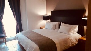 Une chambre d’hôtel avec un grand lit, deux lampes de chevet, une chaise et une fenêtre avec des rideaux.