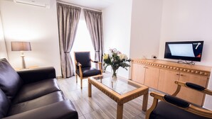 Une chambre d’hôtel moderne avec un canapé en cuir, une table basse en bois, un téléviseur et un meuble de rangement.