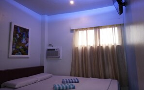 Habitación de hotel con cama, almohadas, un cuadro en la pared, un equipo de aire acondicionado y una ventana con cortinas.