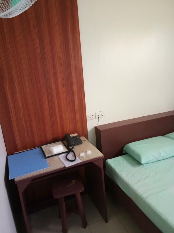 Una habitación pequeña con un escritorio de madera, un teléfono, una carpeta azul y una cama verde.
