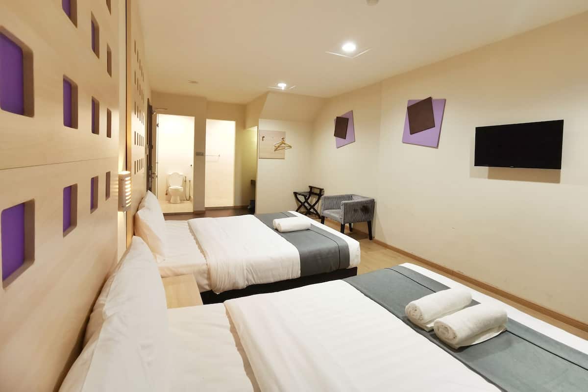 Ein Hotelzimmer mit drei Betten, einem Fernseher, einem Schreibtisch und einem Stuhl.