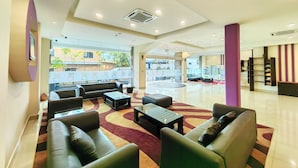 A spacious lobby with leather sofas, a coffee table, and a large window offering a view of the outside. - Hotel 98 (Kuching)