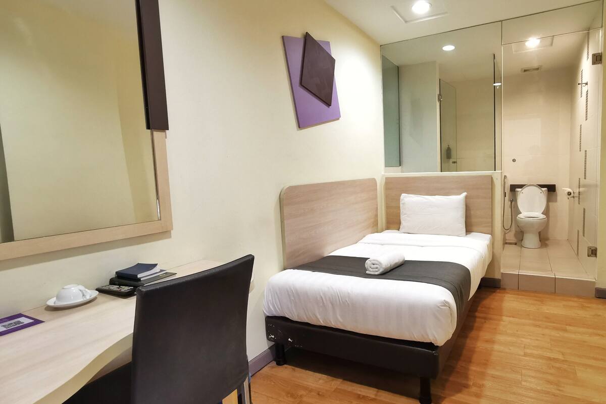 Ein Hotelzimmer mit Bett, Schreibtisch mit Stuhl, Spiegel und einem Badezimmer mit Toilette und Dusche.