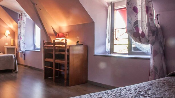 Un dormitorio abrigado en un ático con una cama, una escalera de madera y dos lámparas fijadas a la pared.