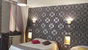 Quarto de hotel com duas camas, papel de parede estampado e luminárias fixadas na parede.