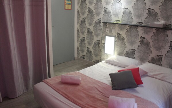 Una habitación de hotel con una cama, almohadas, un estante de vidrio y una cortina.