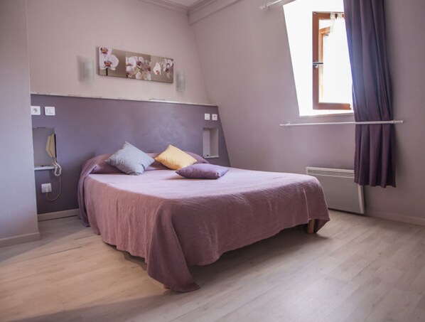Un dormitorio con cama, ventana con cortinas, radiador y teléfono instalado en la pared.