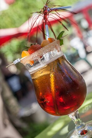 A cocktail in a glass with a straw, garnished with fruit and a mint leaf.