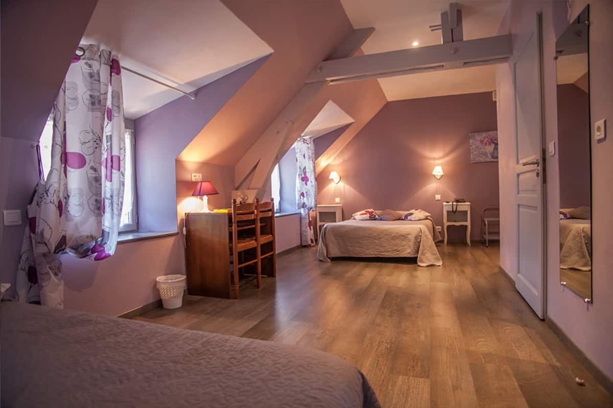 A bedroom with a sloped ceiling, a desk, two beds, and a mirror.