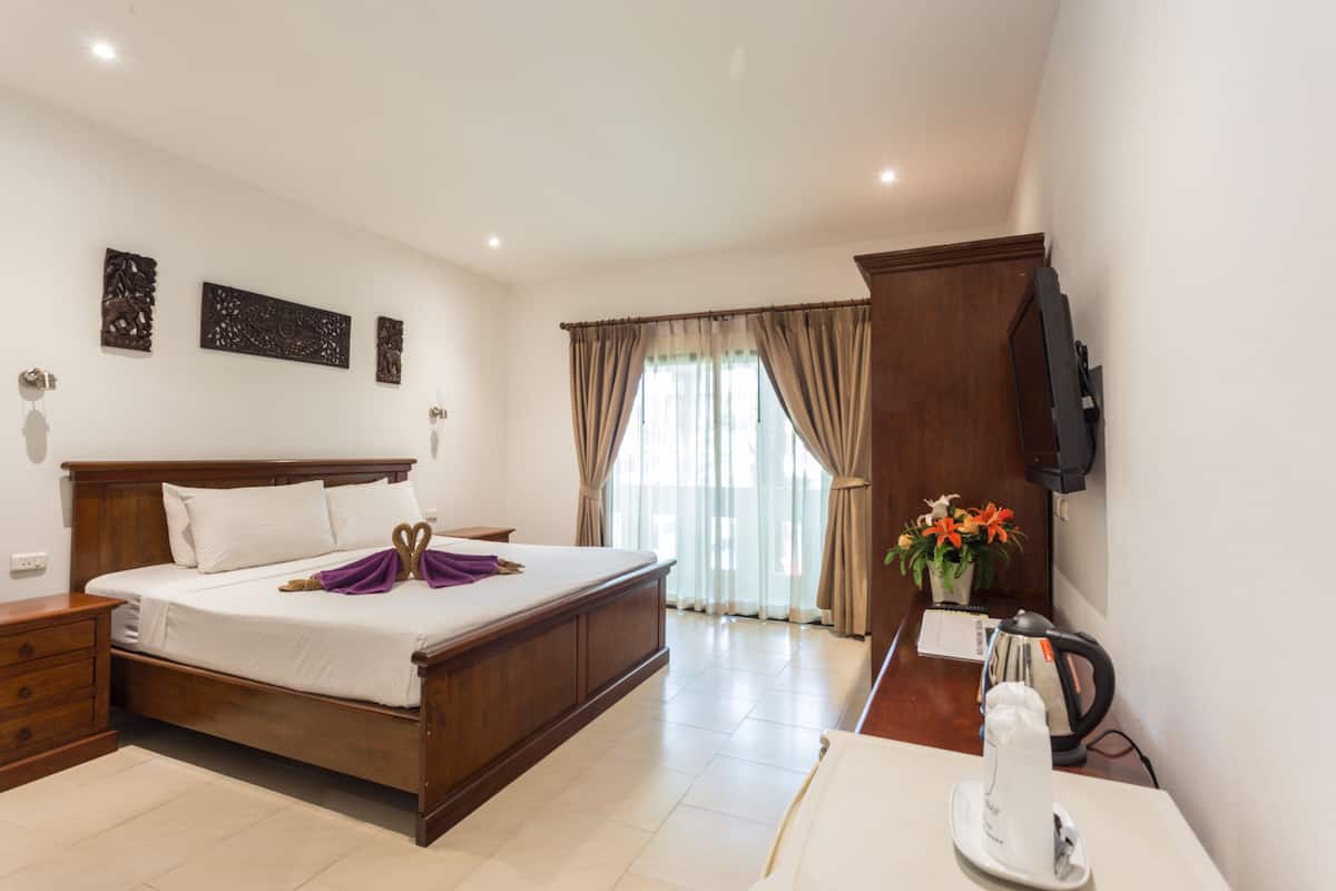 A hotel room with a wooden bed, a desk with a kettle, and a TV on the wall.