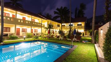 A hotel with a swimming pool, outdoor seating, and palm trees.
