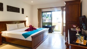 Ein Hotelzimmer mit einem großen Bett, einem Holzschrank, einem Schreibtisch mit Blumenvase und einer Glastür zum Balkon.