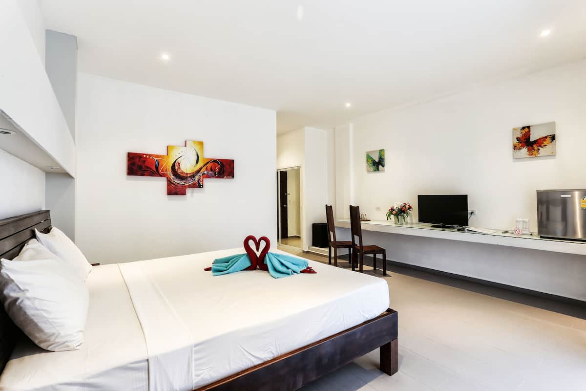 A modern hotel room with a large bed, a desk with a flat-screen TV, and artwork on the walls.