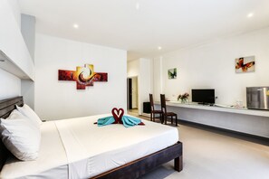 A modern hotel room with a large bed, a desk with a flat-screen TV, and artwork on the walls.