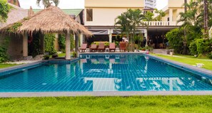 A swimming pool with lounge chairs and a thatched-roof structure.