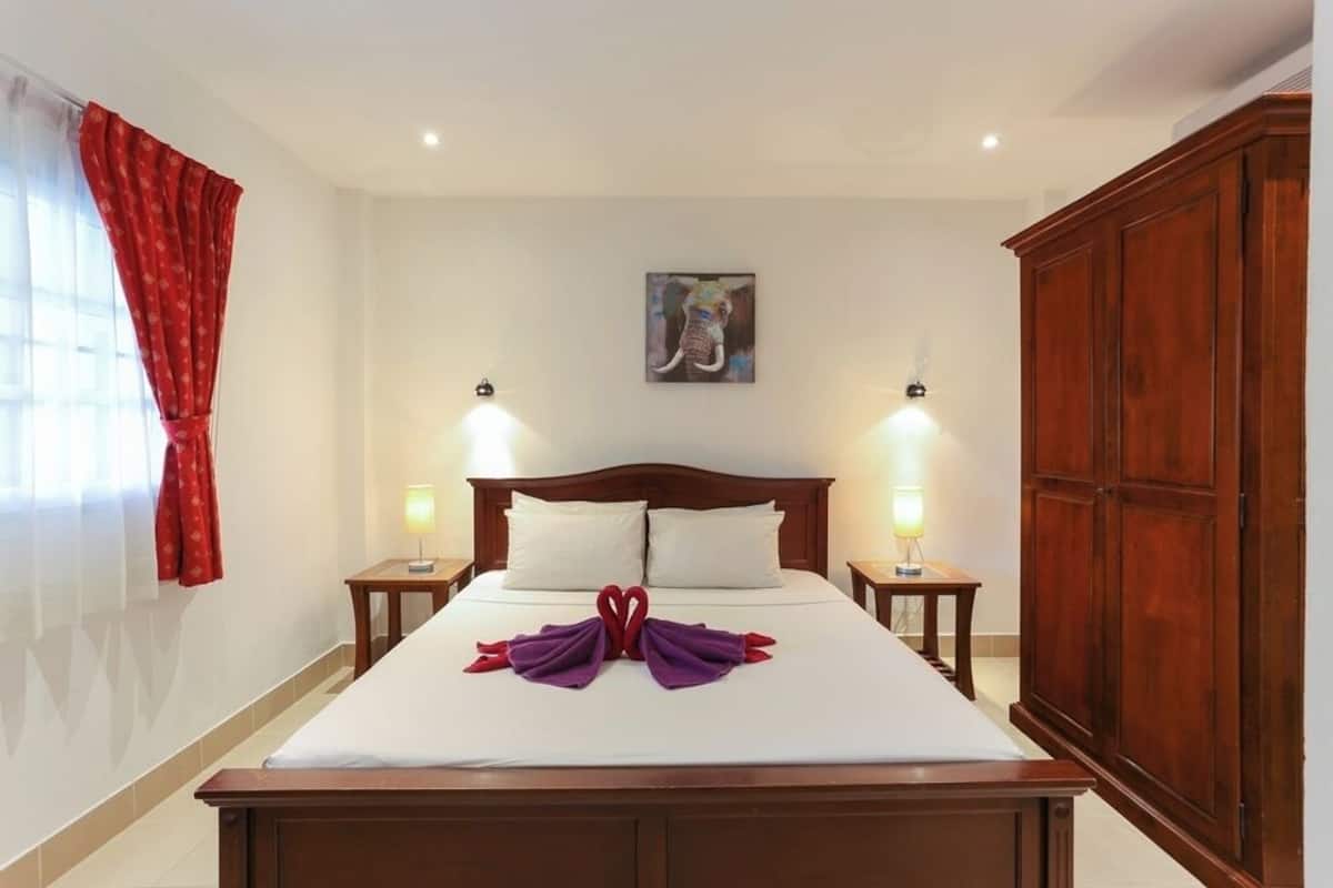 A hotel room with a large bed, two bedside lamps, a wooden wardrobe, and a painting on the wall.