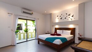Ein Hotelzimmer mit einem großen Bett, einem Holzkopfende, einem Balkon mit Pflanzen und einer Wand mit Vogelmotiven.