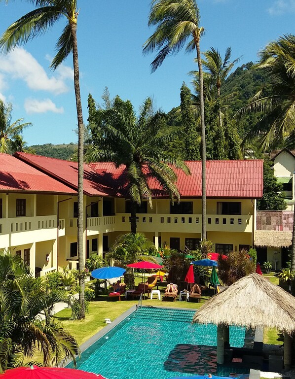 A hotel with a swimming pool surrounded by palm trees and umbrellas.
