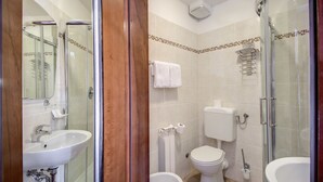 A bathroom with a glass-enclosed shower, a sink, a toilet, and a bidet.