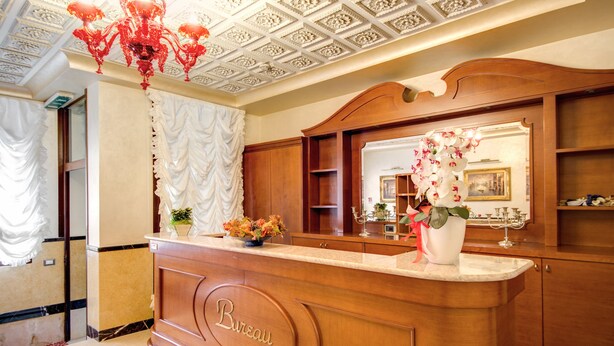 A reception desk with a 'Bureau' sign, a red chandelier, and a mirror reflecting the room.