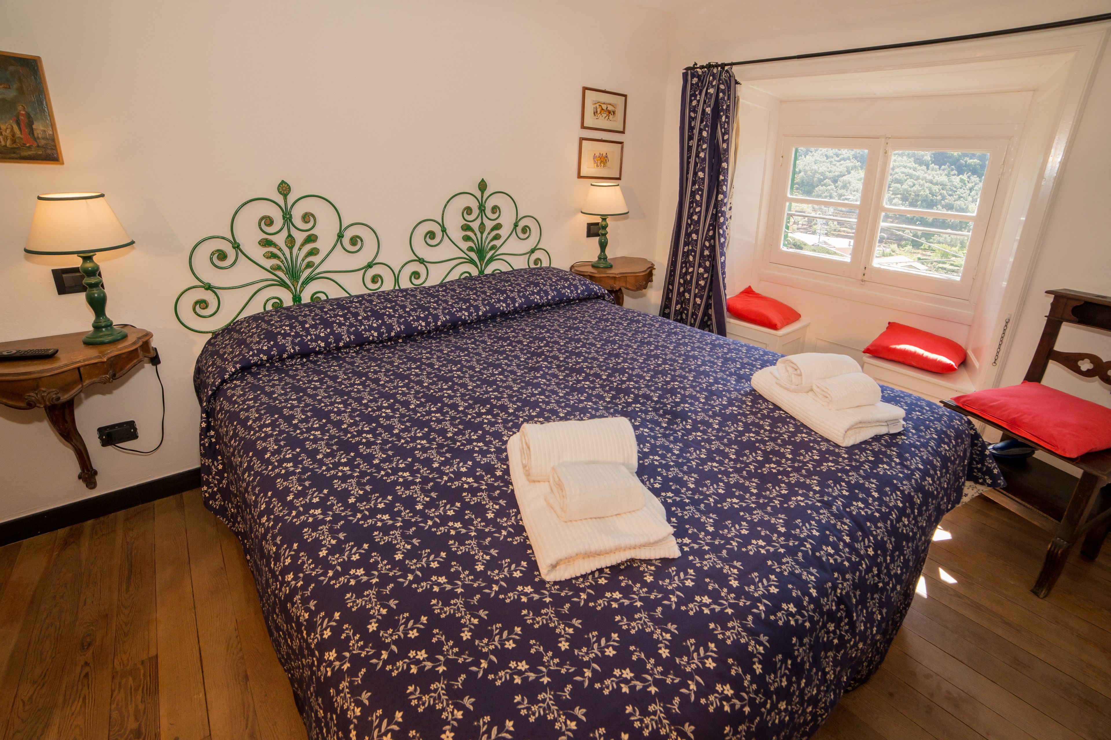 Une chambre à coucher avec une couvre-lit à motifs floraux, deux lampes de chevet, une fenêtre donnant sur un beau paysage et un fauteuil rouge.