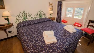 Une chambre à coucher avec une couvre-lit à motifs floraux, deux lampes de chevet, une fenêtre donnant sur un beau paysage et un fauteuil rouge.