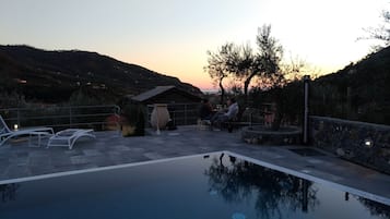 Ein Pool mit Liegestühlen und einem Tisch, umgeben von einer Steinmauer und Blick auf Hügel.