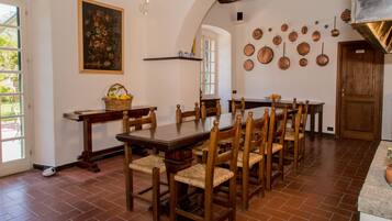 A dining room with a long wooden table, several wooden chairs, a basket on a side table, and a painting on the wall.