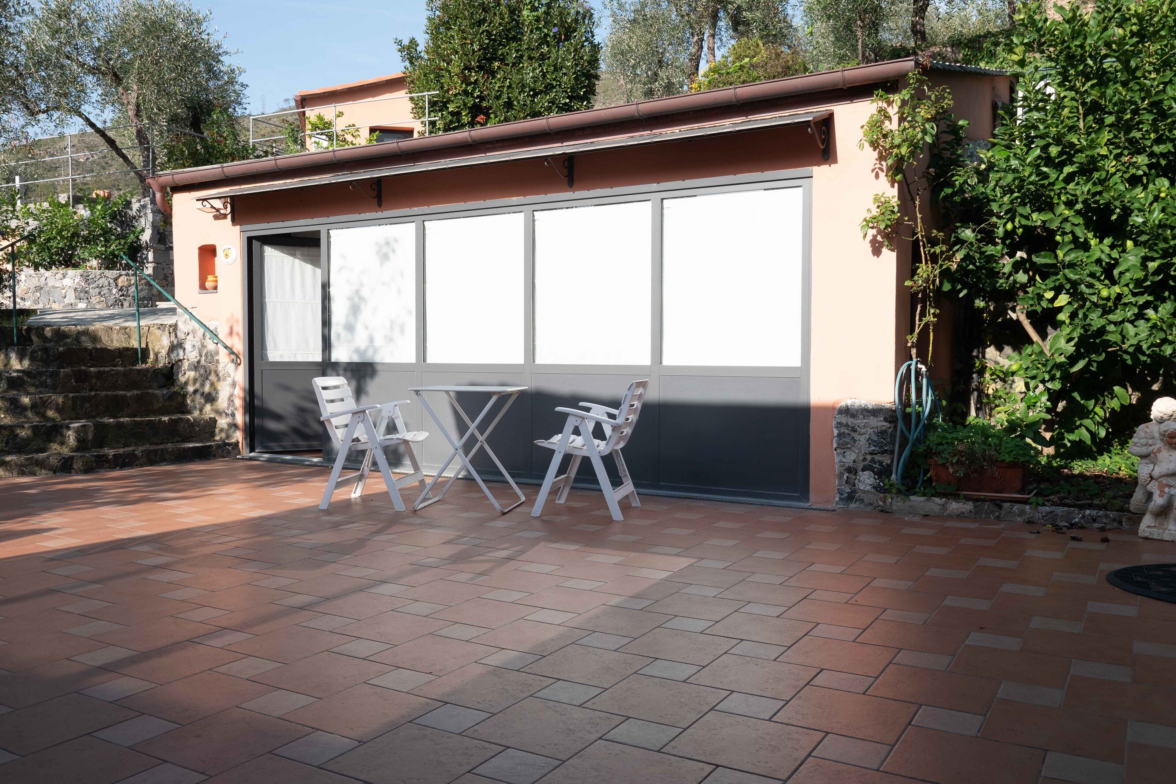 Ein überdachter Patio-Bereich mit Tisch und Stühlen, einer Garagentür und einer Steintreppe.