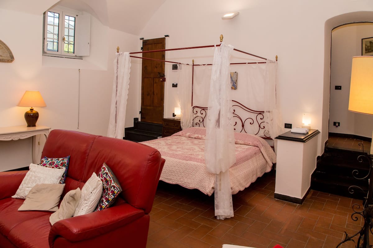 Une chambre à coucher avec un lit à baldaquin, un canapé en cuir rouge et une petite table de chevet avec une lampe.