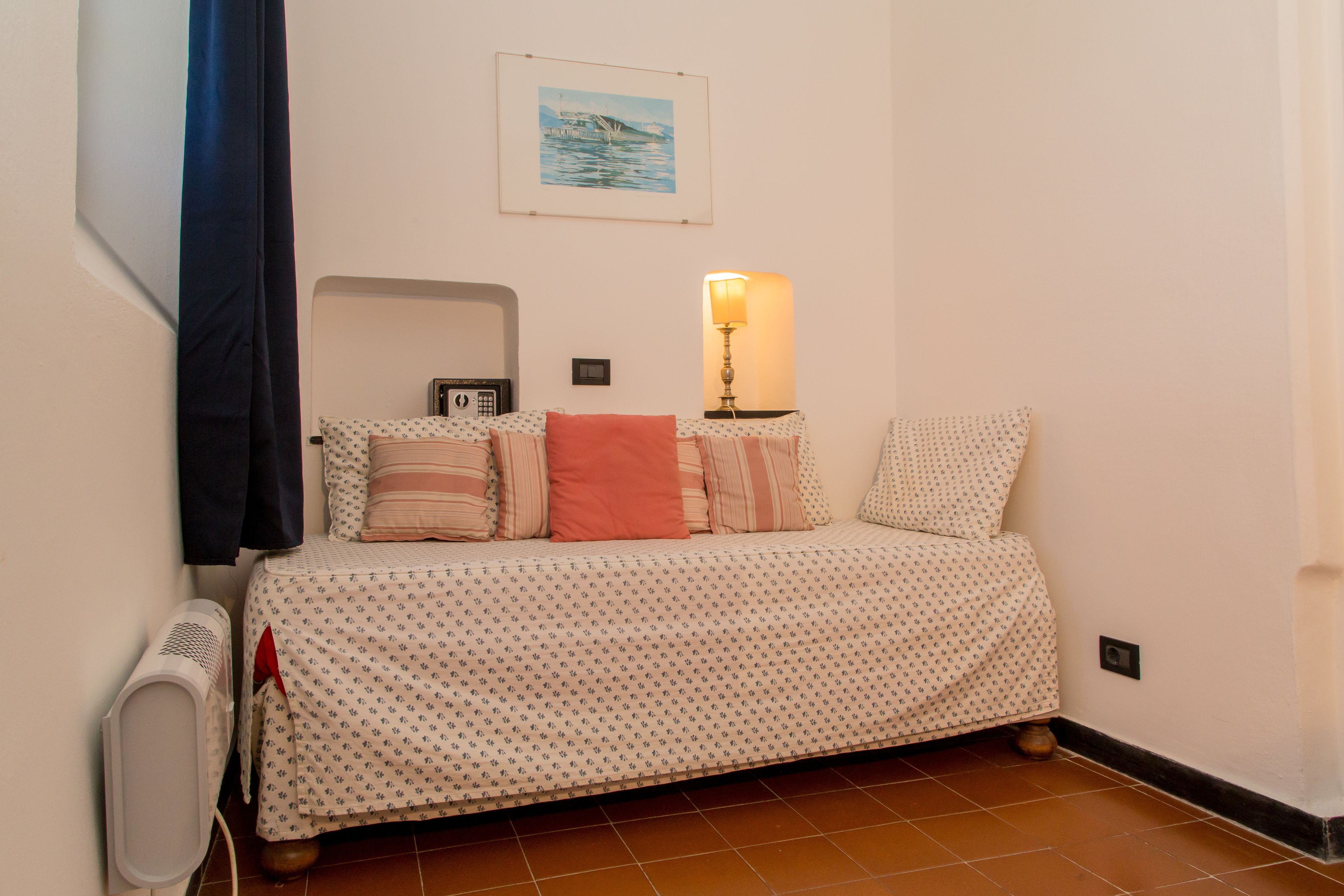 Un dormitorio con cama, lámpara de noche, calefactor y un cuadro colgado en la pared.