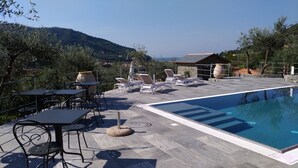 Un espace piscine agrémenté de chaises longues et de tables, entouré de verdure et offrant une vue sur les collines.