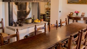 Une longue table à manger en bois, entourée de chaises, une cheminée agrémentée d’un manteau décoratif et un tableau accroché au mur.