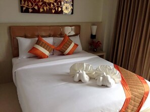 Une chambre d’hôtel avec un grand lit, du linge de lit blanc et des coussins décoratifs orange.