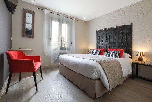 A bedroom with a bed, a red chair, a nightstand, and a wall-mounted mirror. - Le Mas de Castel (Sarlat-la-Canéda)